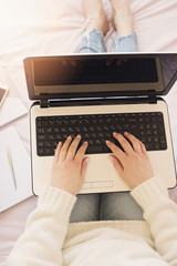 Fototapeta premium Young woman sitting in her bed and using laptop. Feminine workplace concept. Blogger working. Sun haze, glare