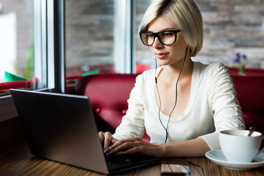 Female Blogger Wearing Glasses While Using Laptop In Cafe