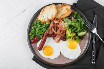 Delicious english breakfast with fried eggs, bacon, toasts and fresh salad
