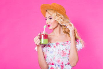 Portrait of young woman holding and drinking tasty green smoothie milkshake on pink background with copyspace