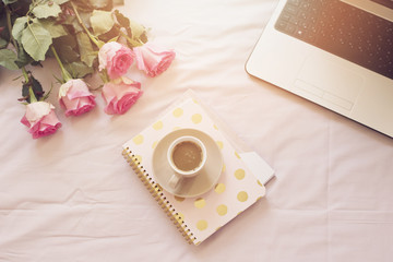 Coffee, old vintage camera in bed on pink sheets. Roses, notebooks and laptop around. Freelance fashion home femininity workspace