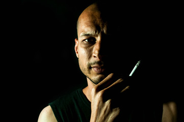 Low key portrait of sweaty man face skin holding smoking cigarette in his hand against black background, not isolated