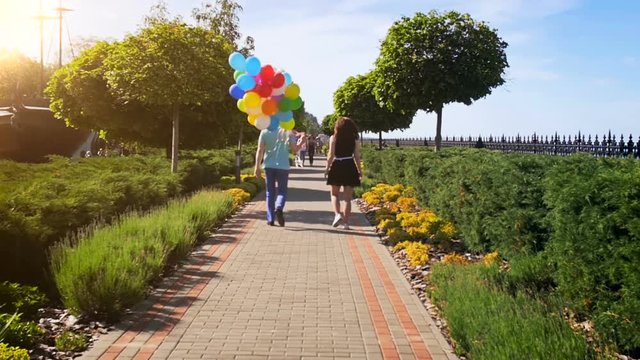 Slow motion video of young couple with bunch of colorful balloons walking at park