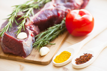Raw beef meat on the wooden cutting board with vegetables, rosemary and spices. Top view. Close up. Food concept.