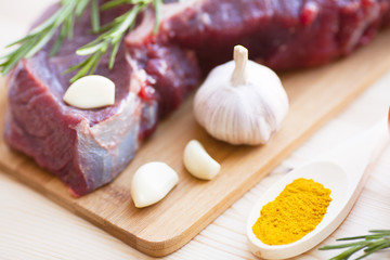 Raw beef meat on the wooden cutting board with vegetables, rosemary and spices. Top view. Close up. Food concept.