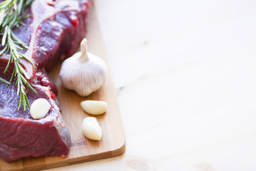 Raw beef meat on the wooden cutting board with vegetables, rosemary and spices. Top view. Close up. Food concept.