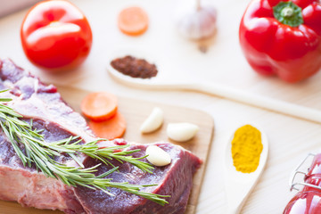 Raw beef meat on the wooden cutting board with vegetables, rosemary and spices. Top view. Close up. Food concept.