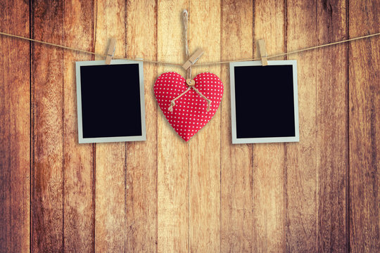 Blank instant photos and red heart hanging on wooden background.