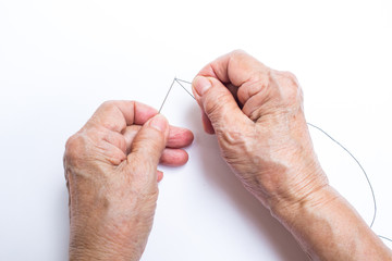 Senior woman's hands finishing to thread a needle isolated on white background, About tailor