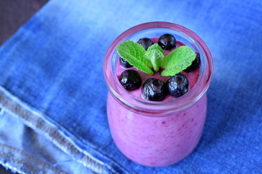 Blueberry smoothie in a glass jar topped with berries and mint against blue background
