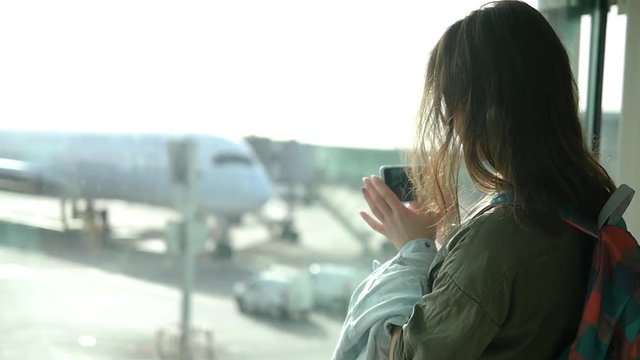 Waiting for the flight - a beautiful girl takes a picture of the plane in the terminal of the airport