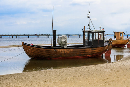 Fischerboot an der Ostsee liegt bei Ebbe am Strand im Hintergrund der Landungssteg