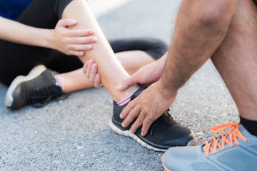 Fototapeta premium Ankle sprained. Young woman suffering from an ankle injury while exercising and running and she getting help from man touching her ankle. Healthcare and sport concept.