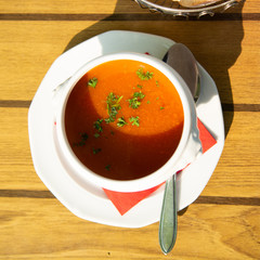 Fresh made vegetables cream soup served in white bowl with bread on outdoor terrace in sunlight