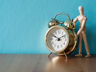 Gold vintage alarm clock on the wood table in the font of wooden puppet stand. the background is blue and copy space for text and content