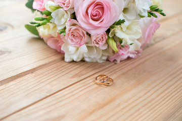 Two gold wedding rings and beautiful wedding are on the brown wood table