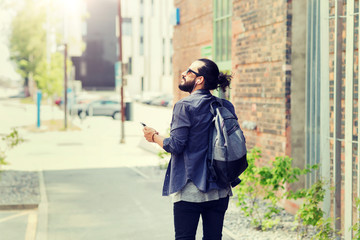 people, technology, travel and tourism - man with earphones, smartphone and bag walking along city street and listening to music 