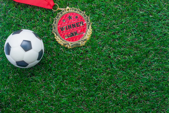 Table top view of soccer or football world cup season background.Flat lay objects gold medal & ball on the artificial green grass wallpaper.Copy space for creative design text and wording content.