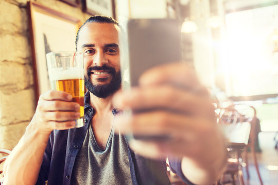 people and technology concept - man with smartphone drinking beer and taking selfie at bar or pub