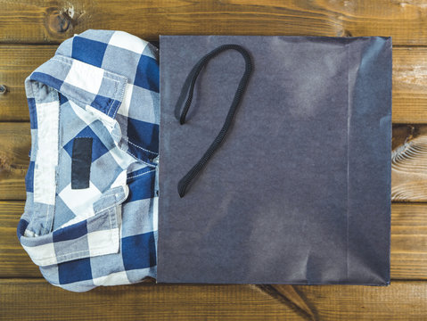 New Checkered Shirt Pop Out From Shopping Bag On A Wooden Background