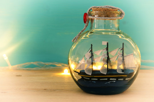 nautical concept image with sail boat in the bottle and gold garland lights over wooden table. Selective focus