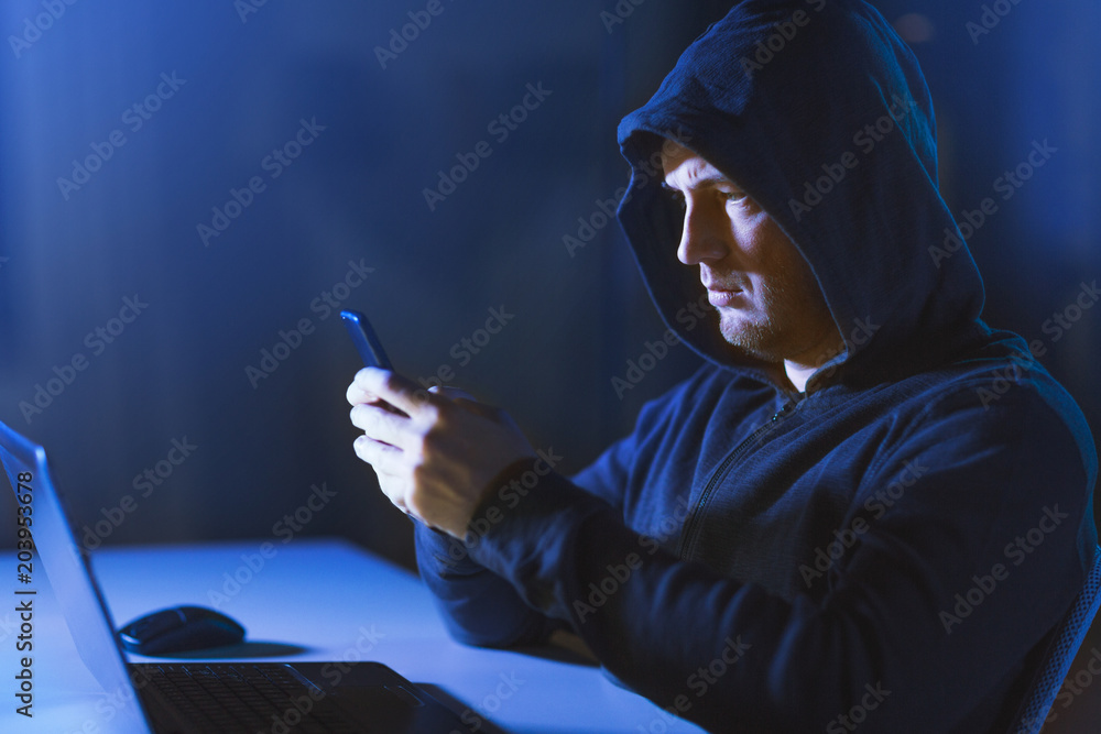 Poster cybercrime, hacking and technology concept - male hacker with laptop computer and smartphone in dark