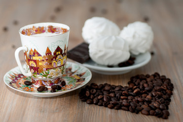 bright cup with coffee beans and sweets on a wooden table