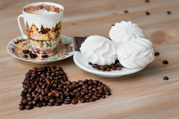 bright cup with coffee beans and sweets on a wooden table