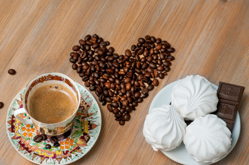bright cup with coffee beans and sweets on a wooden table