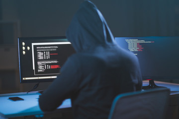cybercrime, hacking and technology concept - male hacker in dark room writing code or using...