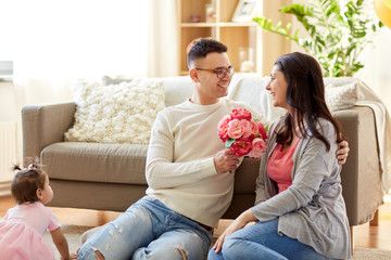 family, holidays and greetings concept - happy husband giving flowers to his wife at home