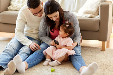 Fototapeta premium family, childhood and technology concept - happy mother, father and little girl with smartphone at home