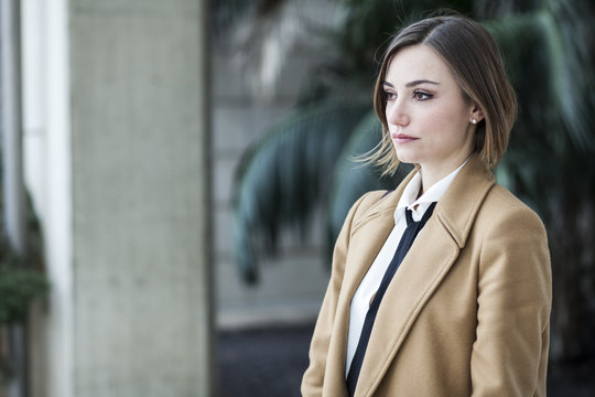 Giovane Manager vestita con cappotto beige camicia  bianca e cravatta nera , che sta in sterni e guarda con aria seria