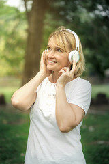 Senior woman listening music with headphone in the park