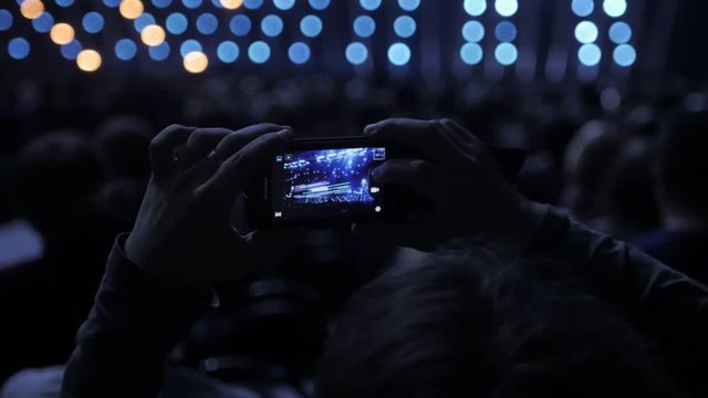 Audience recording video of band on mobile phone in concert.