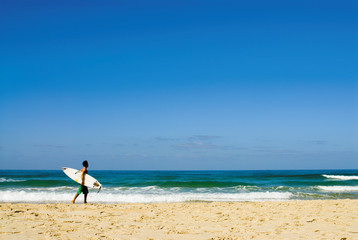 Sandy beach, male person with surfboard walks along beach