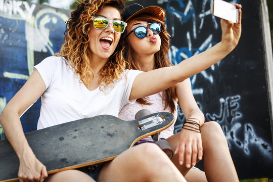 Two female skaters friends sitting on ramp and hangout at the skate park .Taking selfie.