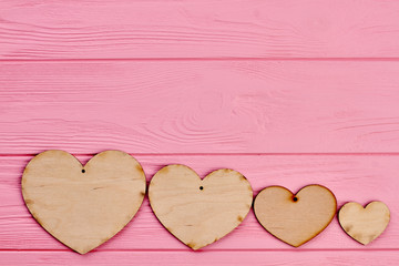 Obraz premium Row of wooden hearts and copy space. Four plywood blank hearts on pink wooden background, text space. Happy Valentines Day.