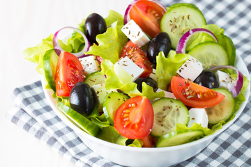 Fresh Greek salad made of cherry tomato, ruccola, arugula, feta, olives, cucumbers, onion and spices. Caesar salad in a white bowl on wooden background. Healthy organic diet food concept.