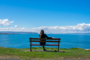 young woman sitting on bench and looking on ocean. relax and enjoy the view. coast of northern Ireland 