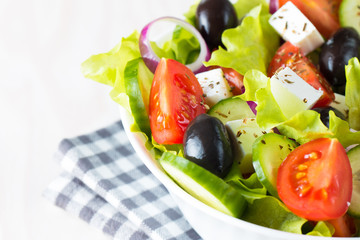 Fresh Greek salad made of cherry tomato, ruccola, arugula, feta, olives, cucumbers, onion and spices. Caesar salad in a white bowl on wooden background. Healthy organic diet food concept.