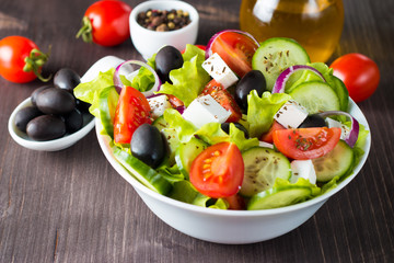 Fresh Greek salad made of cherry tomato, ruccola, arugula, feta, olives, cucumbers, onion and spices. Caesar salad in a white bowl on wooden background. Healthy organic diet food concept.
