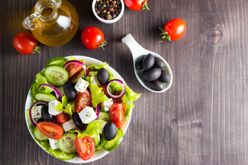 Fresh Greek salad made of cherry tomato, ruccola, arugula, feta, olives, cucumbers, onion and spices. Caesar salad in a white bowl on wooden background. Healthy organic diet food concept.