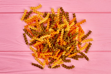 Heap of colorful spiral macaroni, top view. Group of colorful fusilli pasta on pink wooden backgorund. Traditional itatlian food.