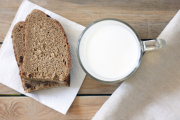 A glass of milk next to a slice of rye bread on the table
