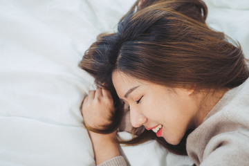 Portrait beautiful young Asian woman on bed at home in the morning. Cheerful Asian woman wearing a comfortable sweater and smiling on her bed. Relaxing room. lifestyle asia woman at home concept.
