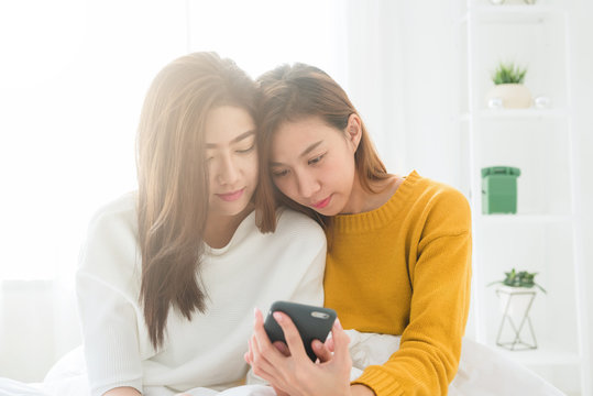 Beautiful young asian women LGBT lesbian happy couple sitting on bed hug and using phone together bedroom at home. LGBT lesbian couple together indoors concept. Spending nice time at home.