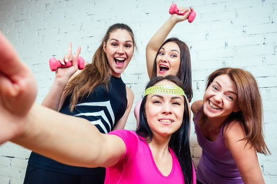four beautiful and young women girlfriends are photographed selfie on the phone in sportswear in the gym. group portrait of a woman selfie having fun.