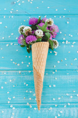 Clover flowers in cone for ice cream on blue background. Top view.