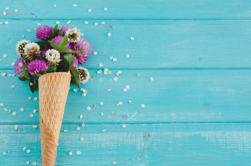 Clover flowers in cone for ice cream on blue background. Top view. Flat lay.